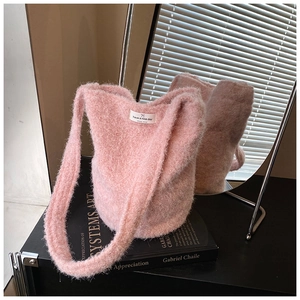 Détail du sac seau en peluche rose avec étiquette carrée posé sur un livre noir