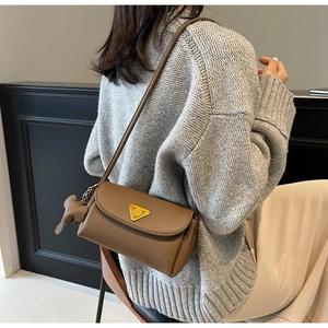 Detail of a brown lychee pattern leather shoulder bag with a gold triangle logo and elephant charm