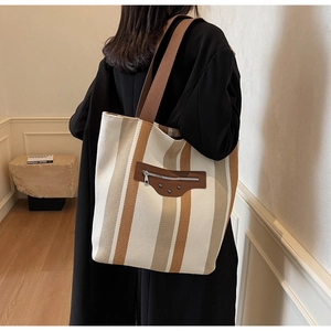 Detail of striped canvas tote bag showing brown leather zipper pocket and vintage studs