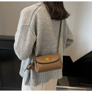 Detail of a brown lychee pattern leather crossbody bag with a gold triangle plate