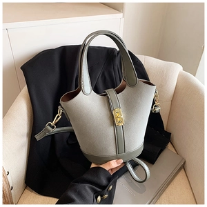 Detail of gray bucket bag with golden twist lock and matte finish on a soft chair