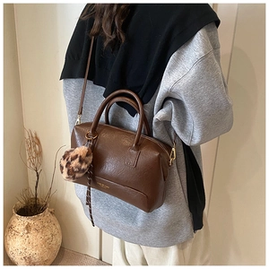 Détail du sac Boston marron foncé avec charm peluche léopard et logo doré sur la bandoulière