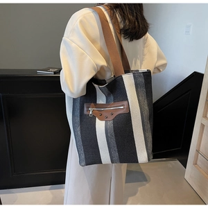 Detail of striped canvas tote bag showing brown leather patch and metallic rivet accents
