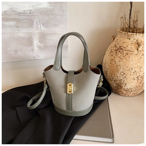 Close-up of light grey bucket bag with golden metal clasp and premium suede texture