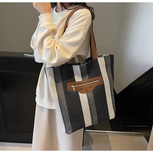 Detail of striped canvas tote bag featuring brown leather patch with silver rivets and zippers