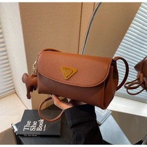Detail of a brown lychee pattern leather handbag with a gold triangle buckle and bear charm