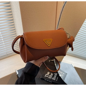 Detail of brown litchi leather crossbody bag with triangular metal logo and horse charm
