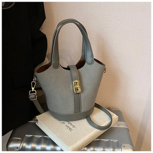 Detail of grey bucket bag with metal buckle and mixed leather texture on silver suitcase
