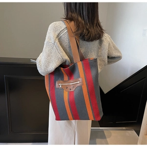 Detail of the high-capacity striped tote bag with leather accent and metal zipper closure