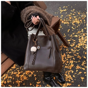 Dettaglio borsa tote in pelle marrone scuro con ciondolo gelato su panca autunnale