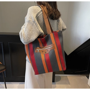Detail of striped canvas tote bag featuring a brown woven strap and premium leather accents