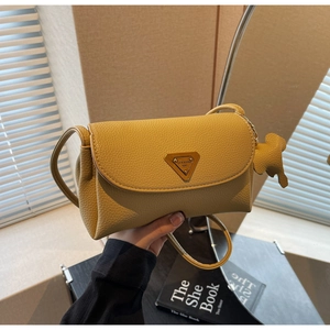 Close-up of yellow pebble leather crossbody bag with metal logo and elephant charm