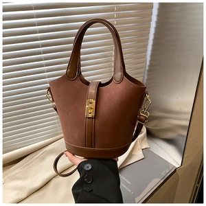 Detail view of brown suede bucket bag with gold clasp and leather trim on minimalist background