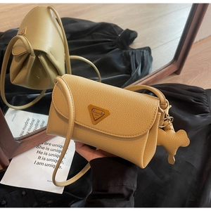 Detailed macro view of beige pebble leather handbag with triangular metal logo and bear charm