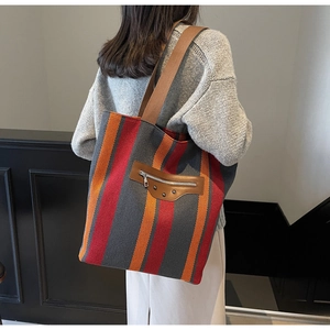 Detailed view of a striped canvas tote bag with brown leather accents and metal rivets