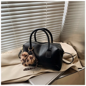 Détail du sac polochon en cuir noir avec fermeture éclair dorée et pompon léopard
