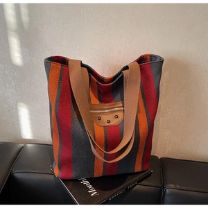Detail of canvas tote bag with vibrant stripes, brown straps, and metallic stud accents
