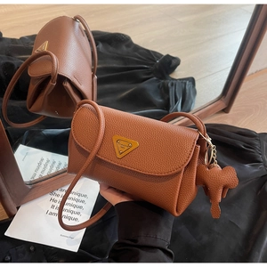 Detail of brown lychee leather crossbody bag with gold triangle plate and elephant charm