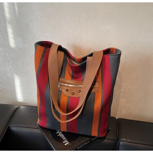 Detailed close-up of striped canvas tote bag with brown leather patches and metal rivets