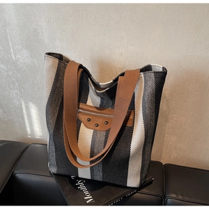 Detailed view of striped canvas tote bag with brown leather handles and metallic studs