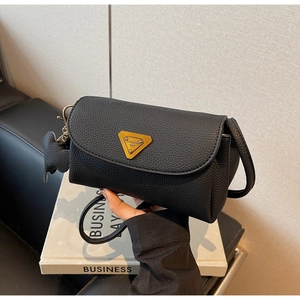 Detail of black lychee grain shoulder bag with gold triangular metal plate and charm