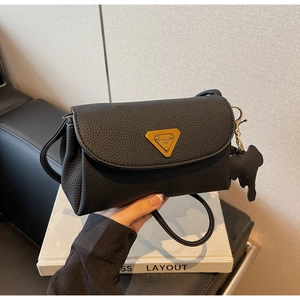 Detail of black lychee leather bag with golden triangular logo and cute dog charm