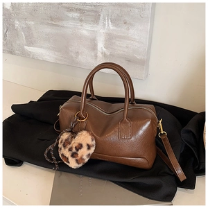 Détail d'un sac polochon marron avec un charme de cœur léopard et des ferrures dorées