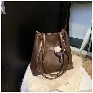Dettaglio della borsa tote in pelle marrone scuro con ciondolo rosa morbido su un tappeto