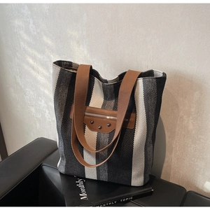 Detail of canvas tote bag showing striped texture and leather pocket with metal studs