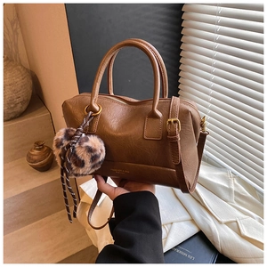 Détail d'un sac Boston marron avec texture en cuir lisse et breloque pompon léopard