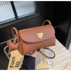 Detail of brown litchi pattern leather bag with gold logo and cute elephant charm