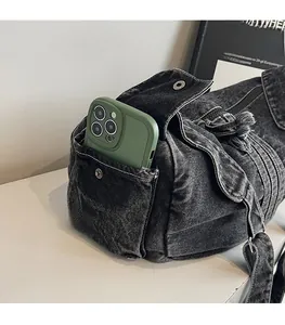 Detail view of a black denim tote bag featuring a practical side pocket with a metal snap
