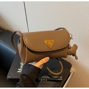 Close-up of coffee brown lychee leather handbag with golden triangle logo and bear charm