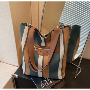 Detail of multi-color striped canvas tote bag with brown leather accents and metal studs