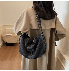 Detail of dark gray washed denim hobo bag with thick decorative stitching and wide strap