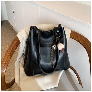 Dettaglio di borsa tote nera in pelle martellata con ciondolo su sedia vintage