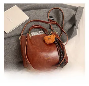 Detail showing the brown vintage tote bag with a plush bear charm and luxury gold hardware