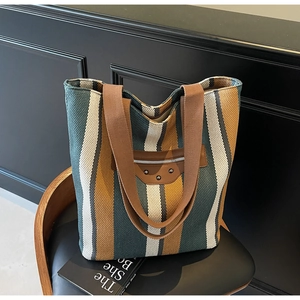 Detail of striped canvas tote bag with brown leather pocket and metallic rivet accents