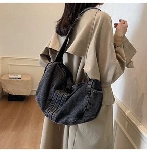 Close-up of a large dark denim hobo bag worn with a beige trench coat for a stylish look
