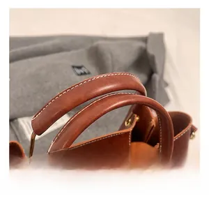 Detail view of smooth dual handles on a brown leather handbag with gold metal hardware