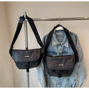 Detail of black nylon messenger bag with adjustable shoulder strap and brand logo label