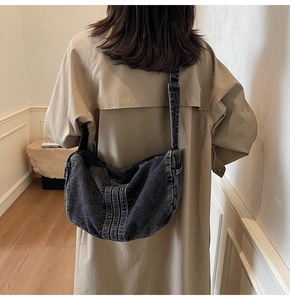 Detailed view of grey washed denim half-moon crossbody bag with wide shoulder strap and stitching
