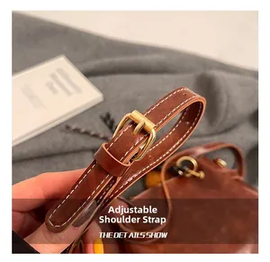 Detail of adjustable dark brown leather shoulder strap with gold buckle and white stitching