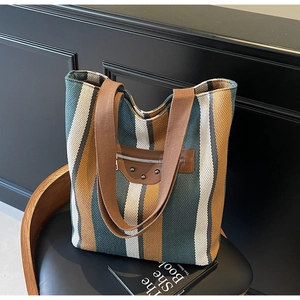 Detail of striped canvas tote bag with brown leather accents and metal rivet studs