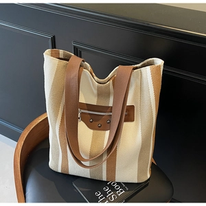 Detail of striped canvas tote bag with brown leather patches and metallic rivets