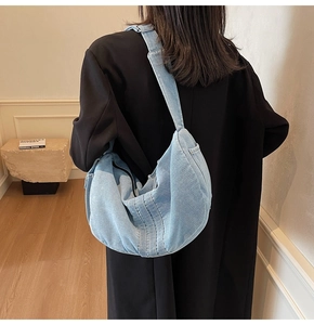 Rear view of a light blue denim crescent crossbody bag on model with wide strap and zip