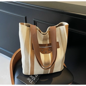 Close-up of striped canvas tote bag featuring vintage brown leather patches and metal studs