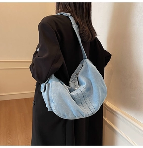 Close-up of light blue denim crescent shoulder bag showing stitching and metal zipper detail