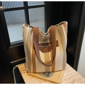 Detail of canvas tote bag with striped texture, leather pocket, and moto-style silver rivets