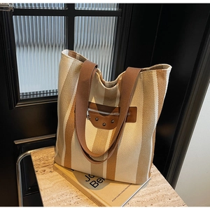 Detail of striped canvas tote bag with brown leather zipper pocket and vintage rivets